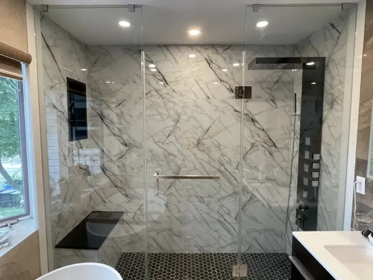 an image about Modern bathroom with a glass-enclosed marble shower and hexagonal black floor tiles.
