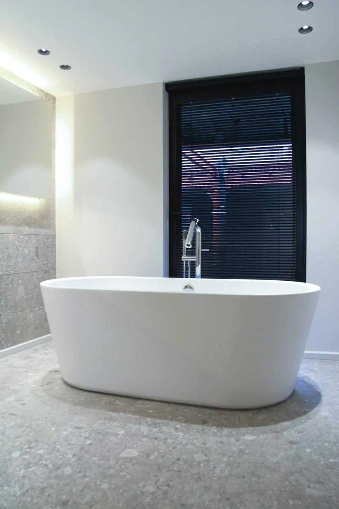 an image about Modern freestanding bathtub in a minimalist bathroom with gray tiles and natural lighting.