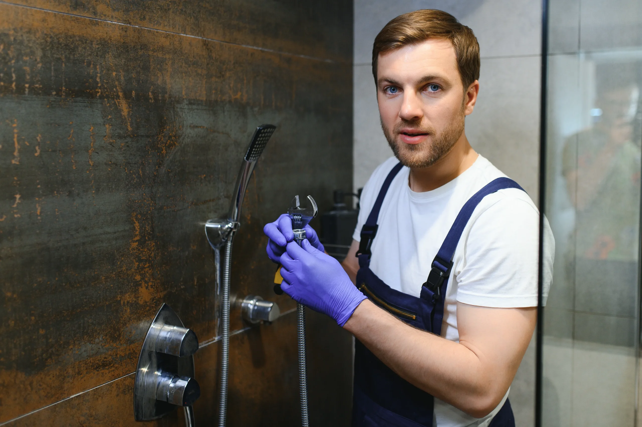 an image about A man in a blue shirt is cleaning a shower in one of the cities.