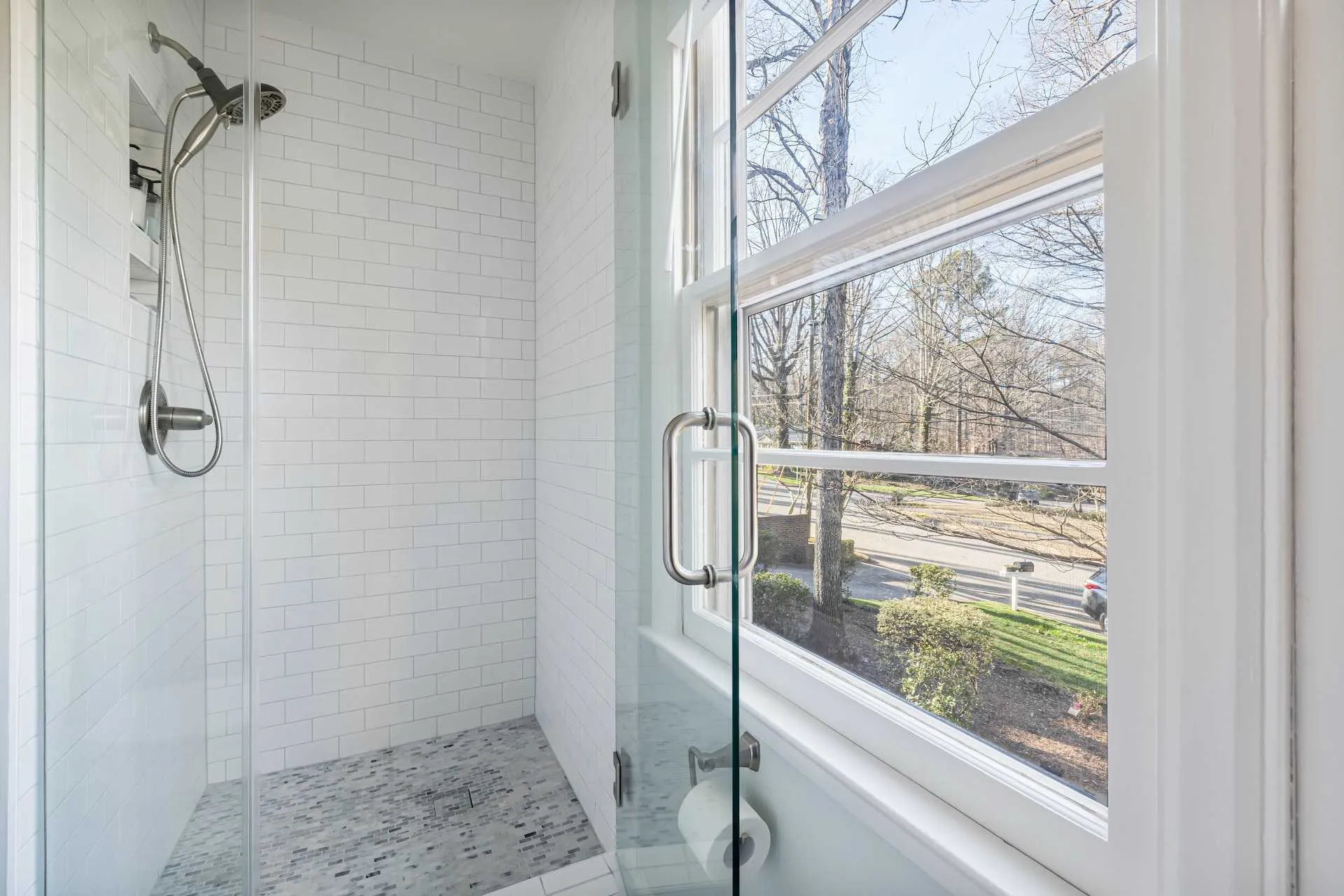an image about An image about a bathroom with a glass shower door and a view of a tree.