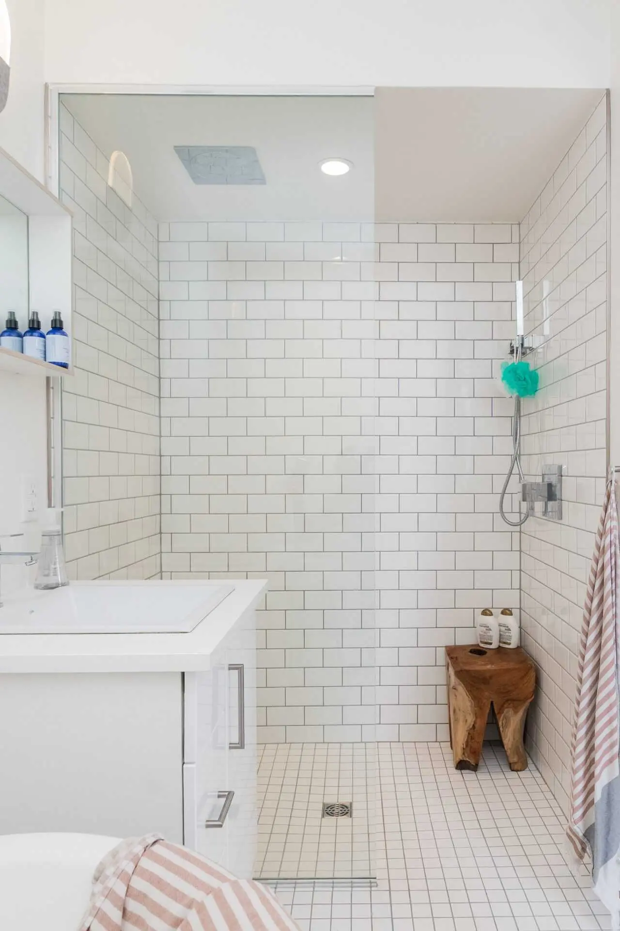 an image about Modern bathroom with white subway tiles, walk-in shower, and wooden stool.